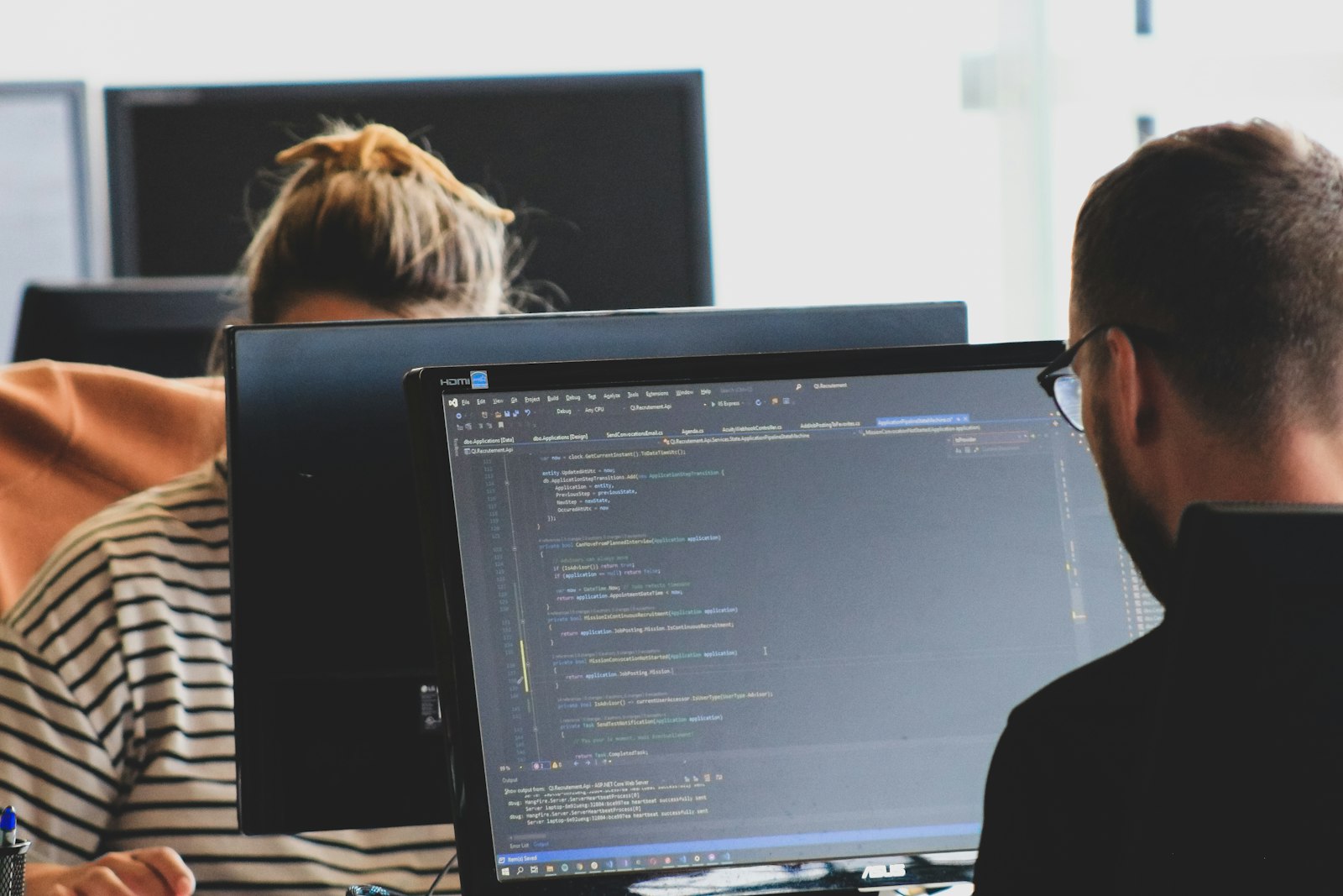 Two engineers writing code at monitors in a bright office